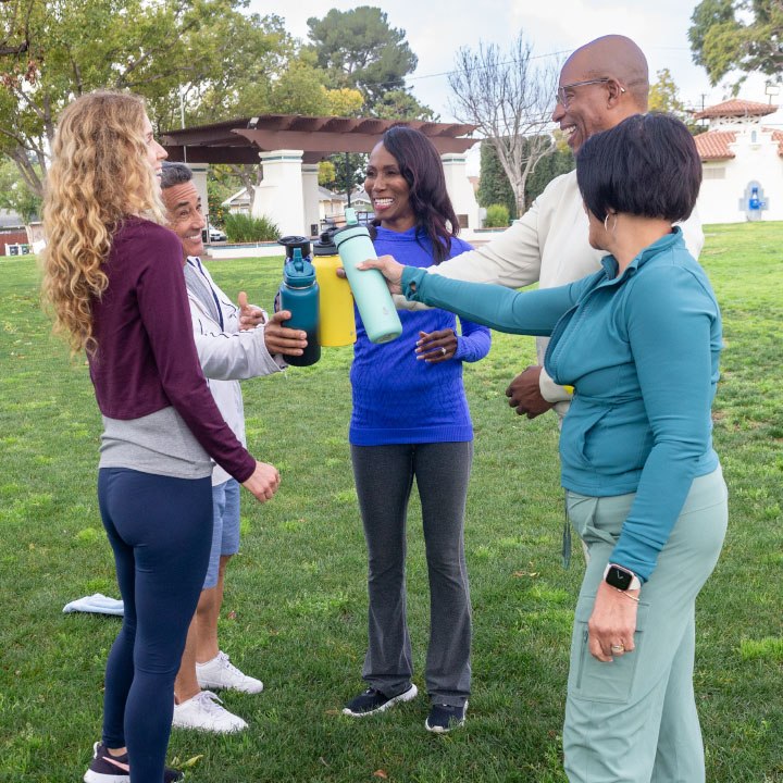 A group of TruStage insured friends working out in a park clank their water bottles together.