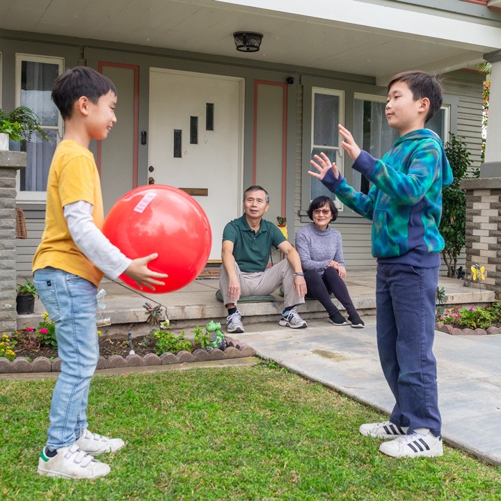 Feeling protected with the right property insurance, two grandparents sit on a porch and watch their two grandchildren play.