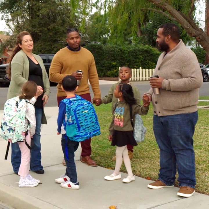 Parents stand with their children at the bus stop, discussing what happens when term life insurance ends.